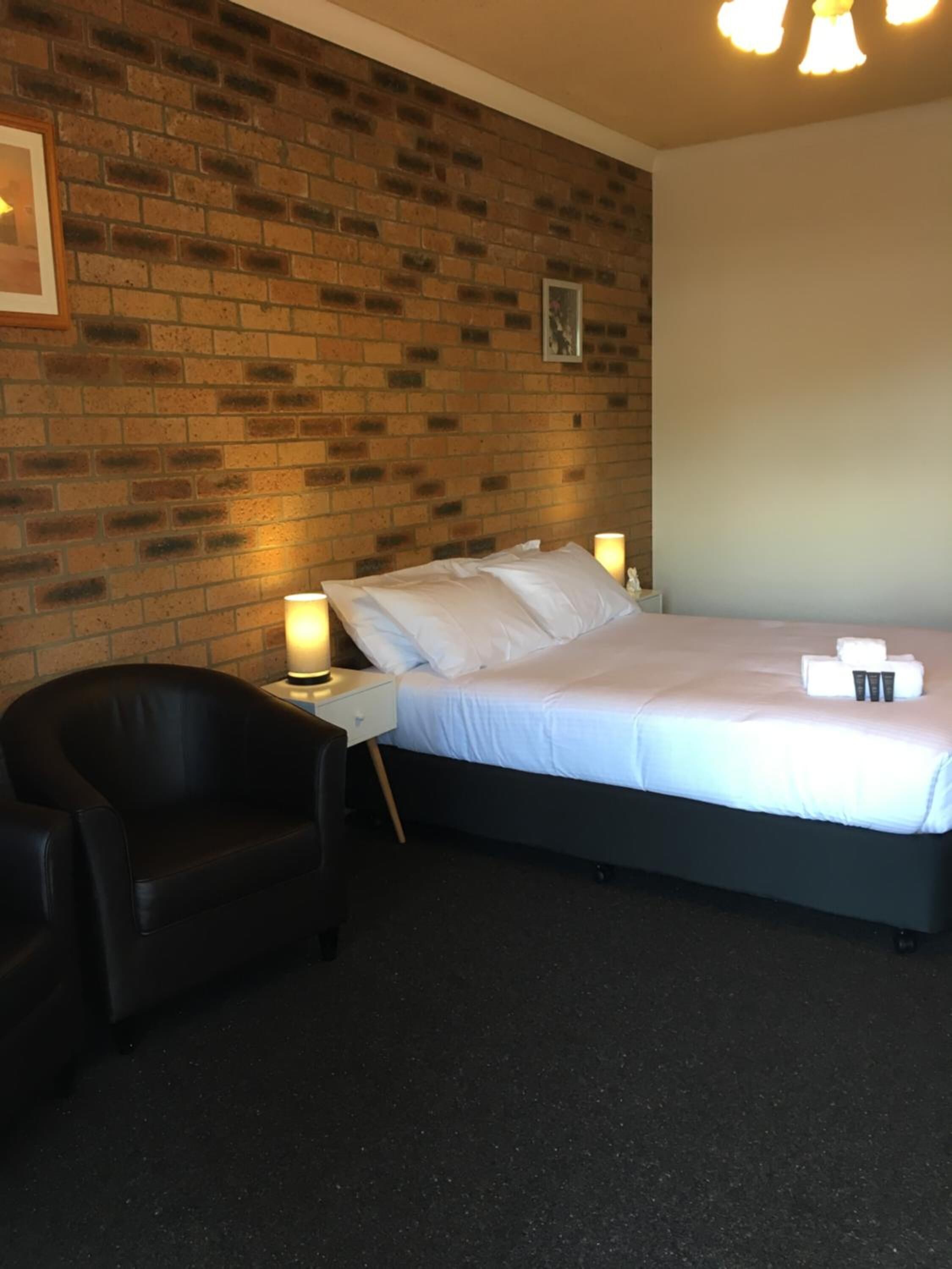 Ein Hotelzimmer mit Ziegelwand, einem Bett mit weißen Leinentüchern, einem schwarzen Ledersessel und Nachttischlampen.