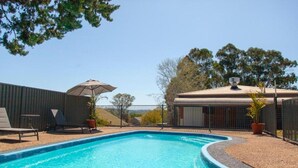 A swimming pool with lounge chairs and an umbrella, surrounded by a fenced area with a building in the background. - Bega Downs Motor Inn (Bega)