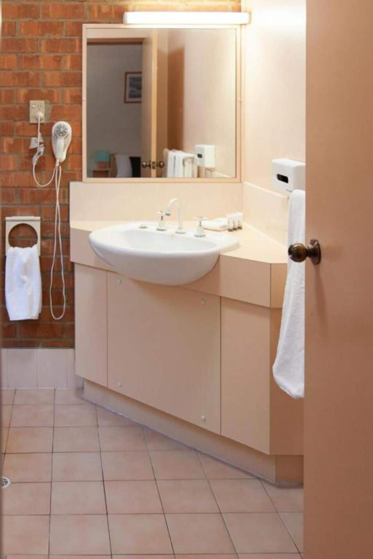 Un baño con lavamanos blanco, un espejo y un perchero para toallas.
