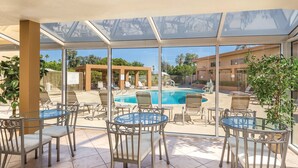Un espacio al aire libre cubierto con piscina, sillones de descanso y mesas.
