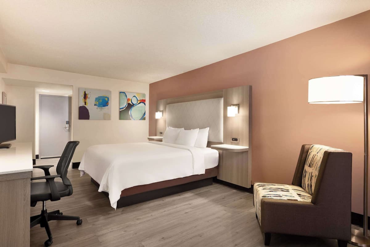 A hotel room with a large bed, a desk with a chair, a sofa, and artwork on the walls.