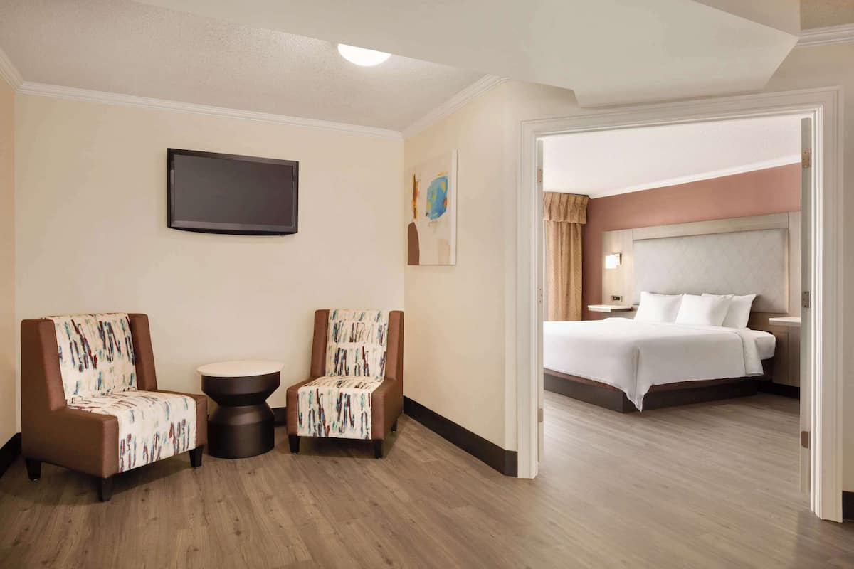 A hotel room with a bed, two armchairs, a round table, and a flat-screen TV mounted on the wall.