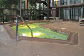 An indoor swimming pool with a tiled floor, metal handrails, and a bench.