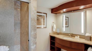Een moderne badkamer met een marmeren douche, een grote spiegel en een houten wastafelmeubel met een wastafel en handdoekrek.