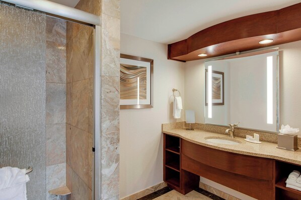 A modern bathroom with a marble shower, a large mirror, and a wooden vanity with a sink and towel rack.