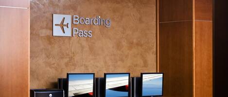 Un mostrador de recepción con un cartel que dice 'Boarding Pass', varias pantallas y una impresora Dell.
