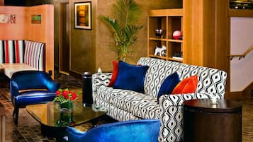 A modern living room with a patterned sofa, a blue armchair, a glass coffee table, and a potted plant.