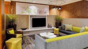 Un salon moderne avec un canapé, des fauteuils, un téléviseur à écran plat et des plantes décoratives.