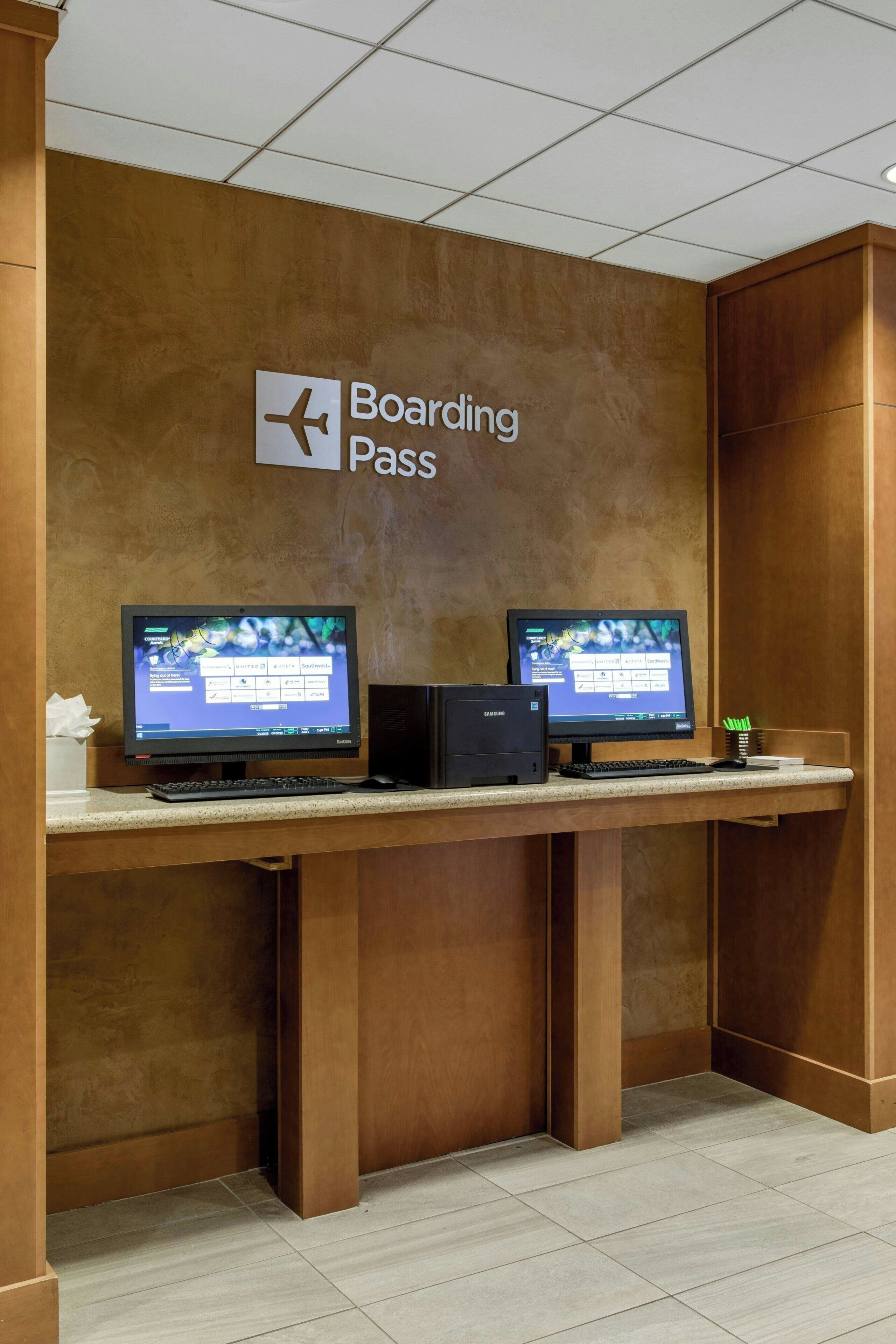 Een incheckbalie met twee monitoren, een bord met 'Boarding Pass' en een kleine plant op de balie.