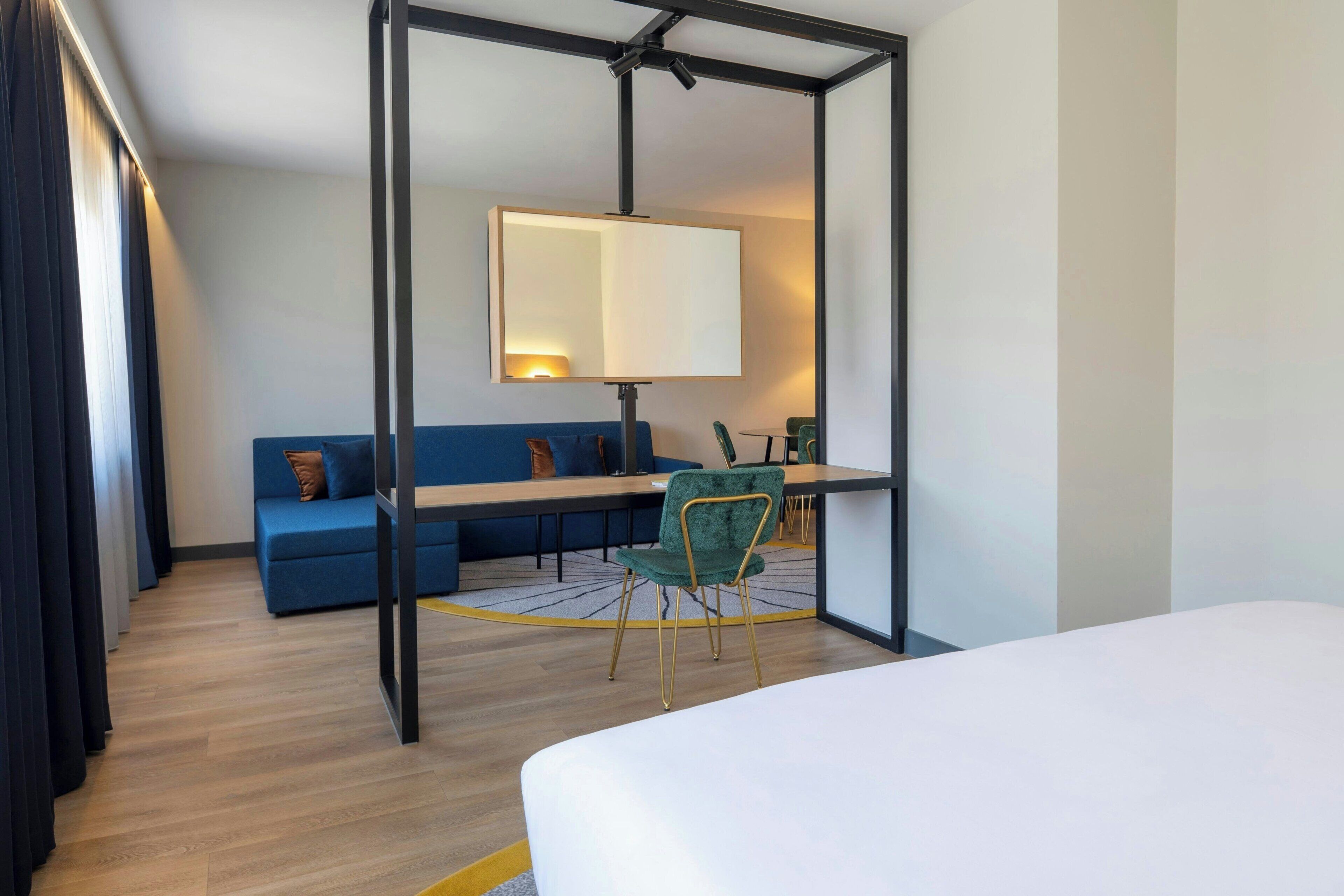 A hotel room with a bed, a desk, a chair, a sofa, and a large mirror.