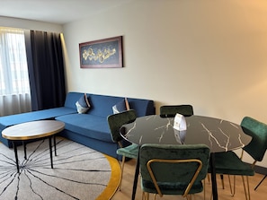 Una sala de estar moderna con un sofá azul, una mesa redonda y sillas verdes.