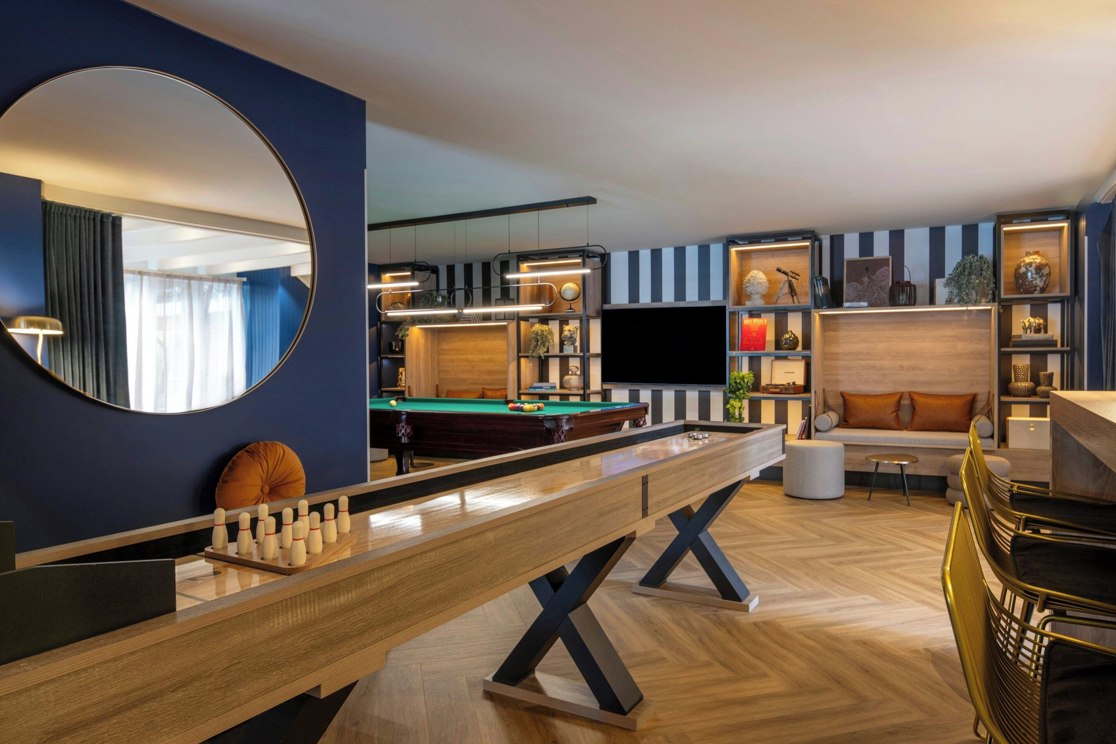 A modern living room with a pool table, a billiards table, and a comfortable seating area with a sofa and ottoman.