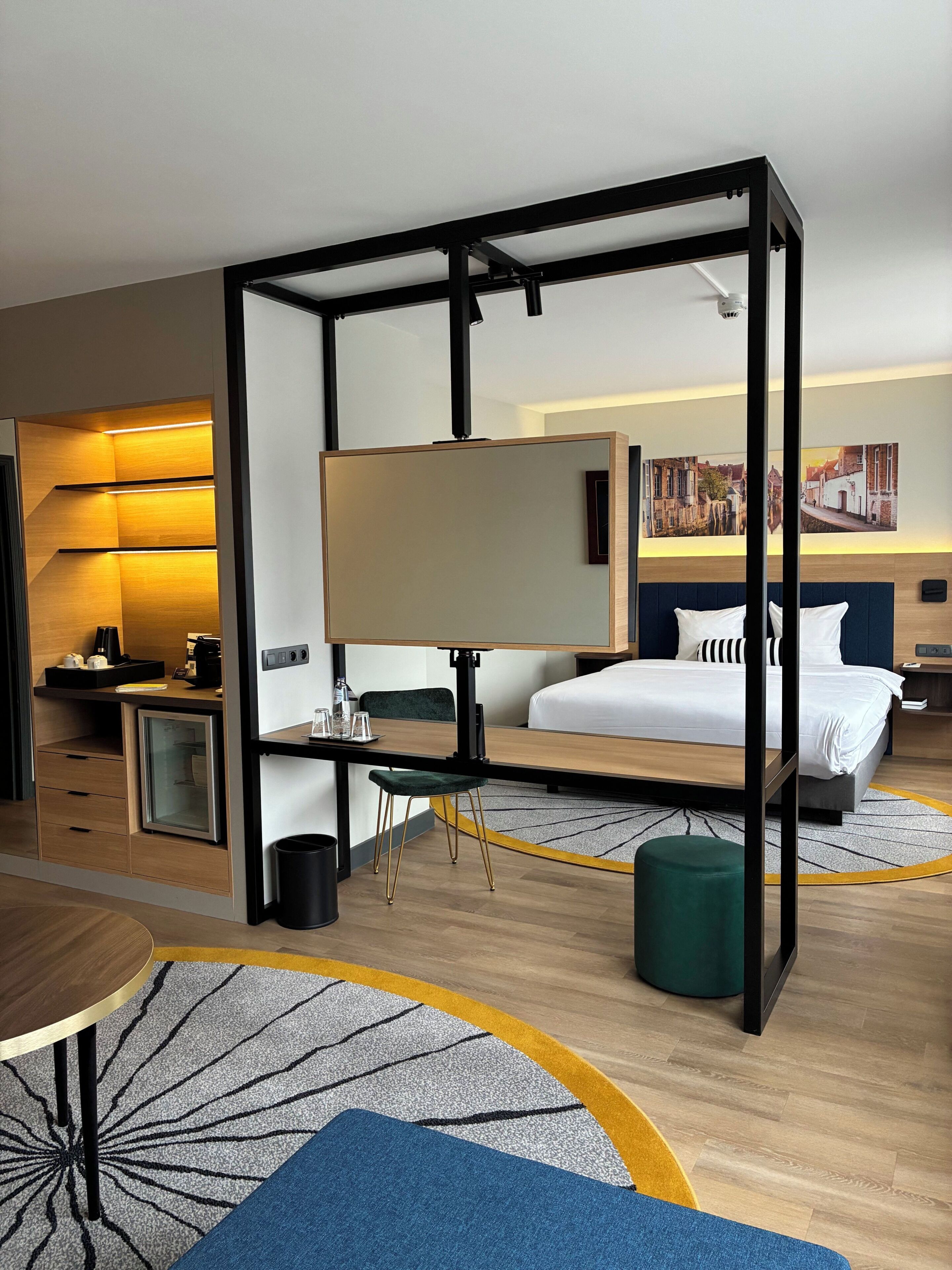 A modern hotel room with a bed, desk, chair, and a large mirror.