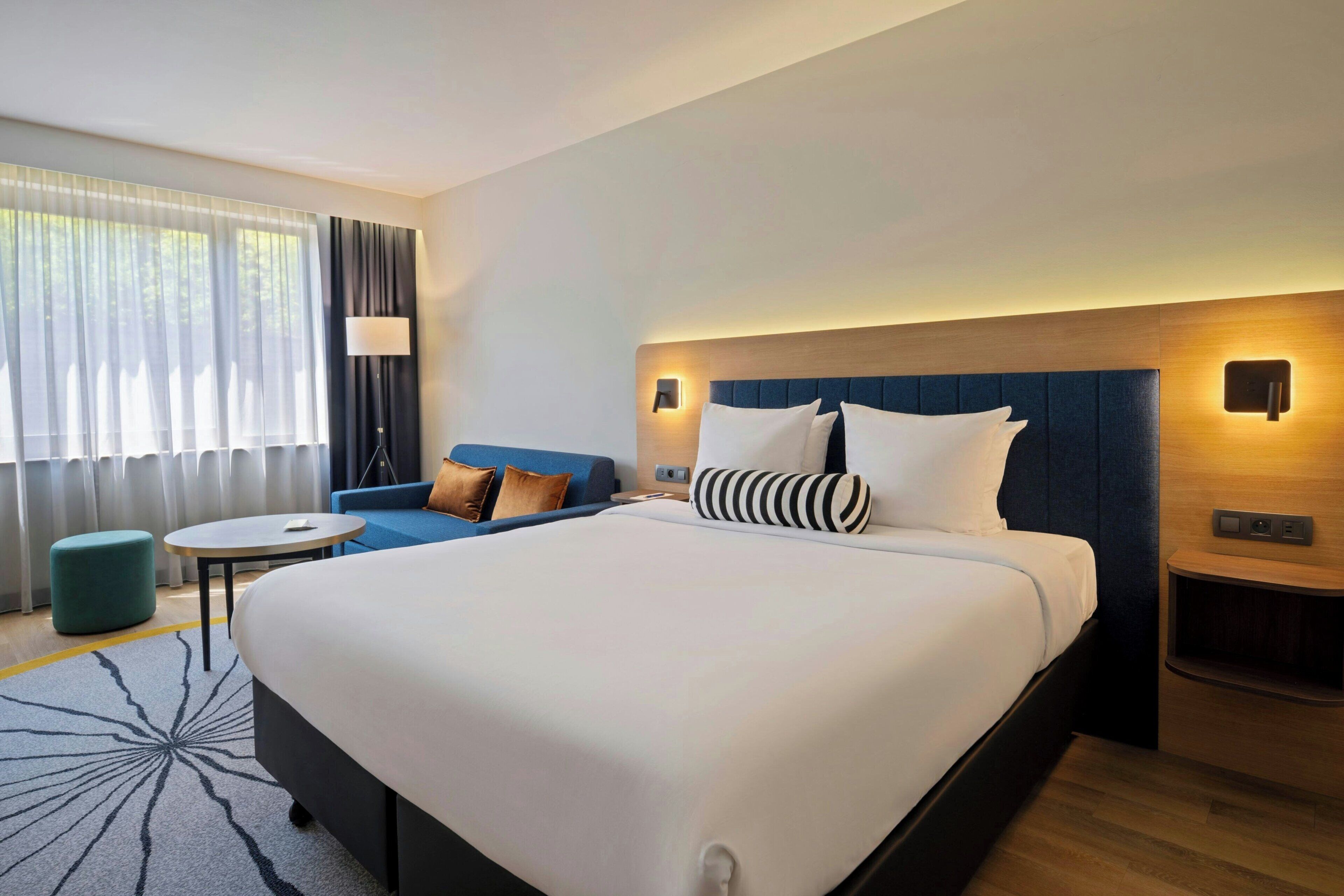 Una habitación de hotel con una cama grande, un sofá, una mesita y una lámpara.