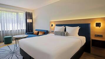 Quarto de hotel com uma cama grande, um sofá, uma mesa pequena e uma luminária.