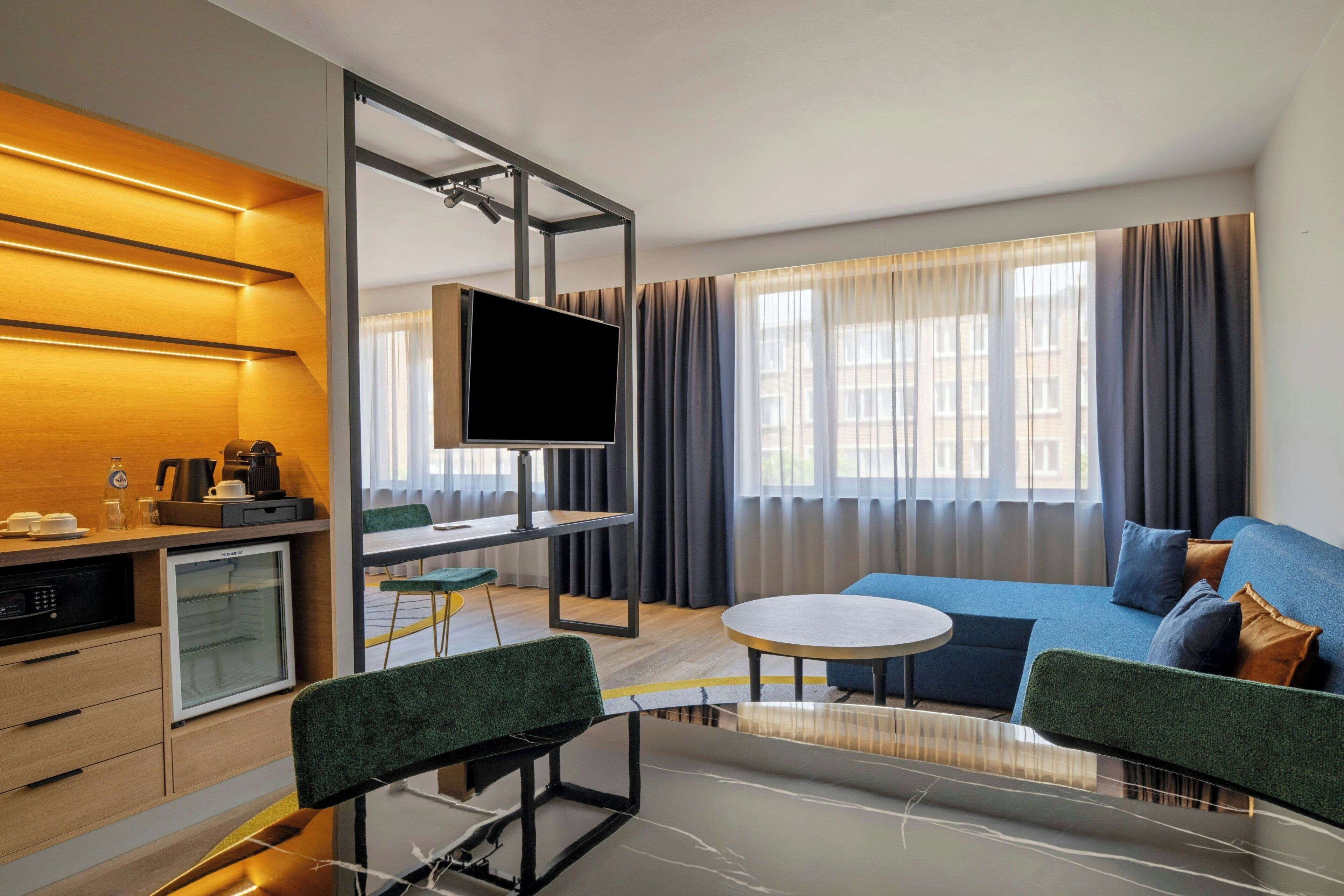 Een moderne hotelkamer met een flatscreen televisie, een bank, een eettafel en een kitchenette.