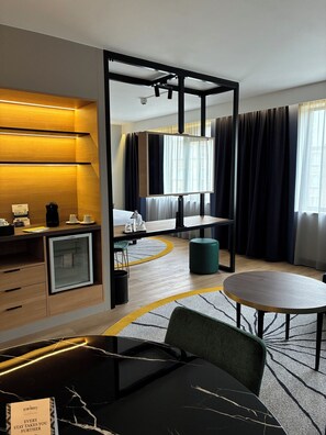 Ein Hotelzimmer mit Bett, Schreibtisch mit Computer, kleinem Kühlschrank, rundem Tisch und Stuhl.