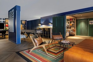 A modern living room with a pool table, leather chairs, and a bookshelf.