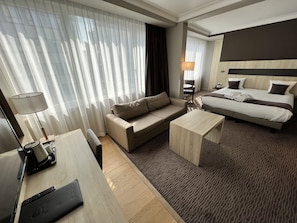 Een moderne hotelkamer met een bank, een bed, een bureau en een lamp.