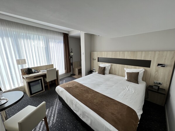 A hotel room with a large bed, a desk, a chair, a TV, and a bedside table.
