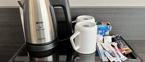 Una bandeja con una cafetera de bajo consumo, dos tazas blancas y una caja de leche para café.