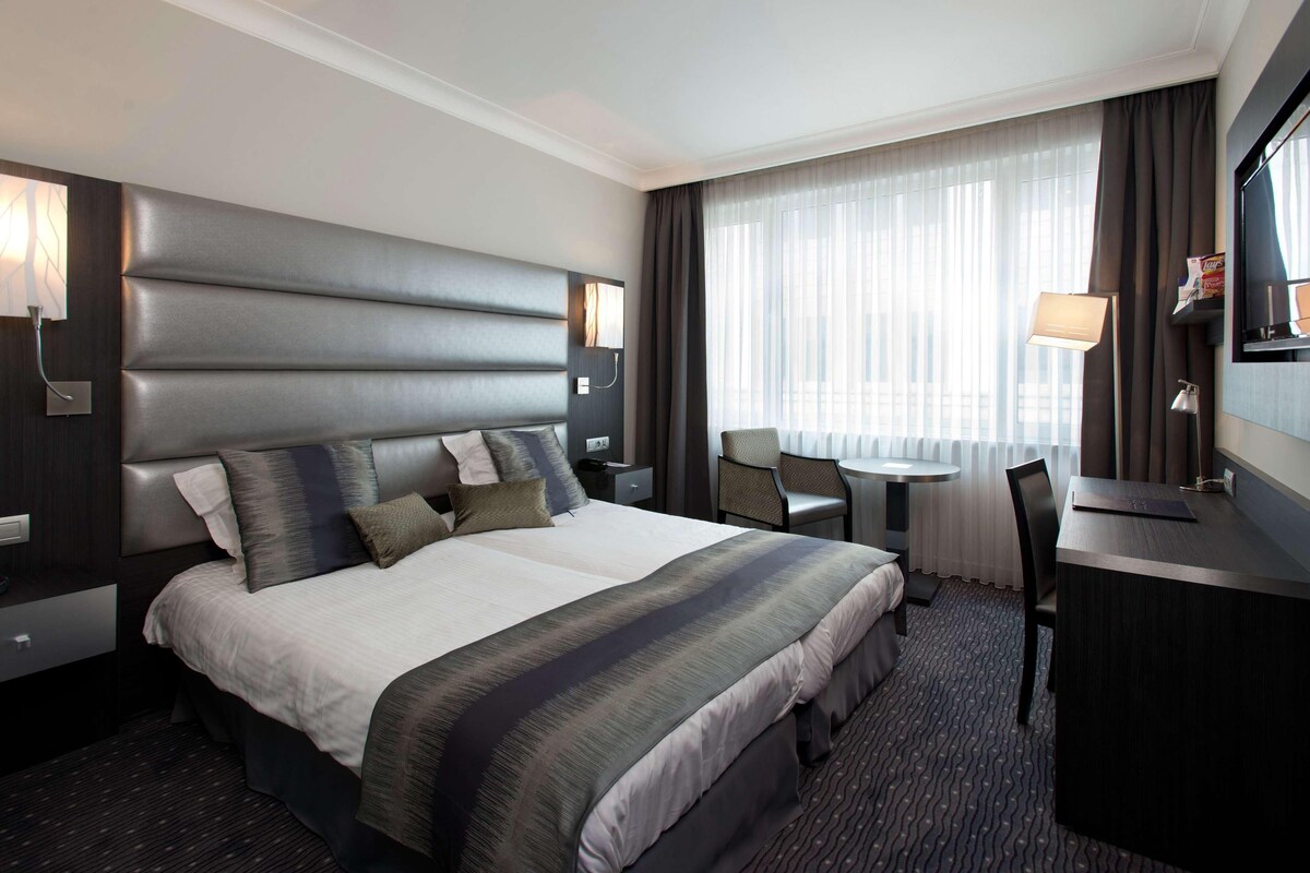 A modern hotel room with a large bed, a desk, and a chair.