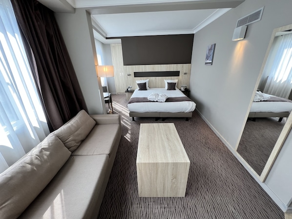 Une chambre d’hôtel avec un lit, un canapé, une table basse en bois et un miroir.