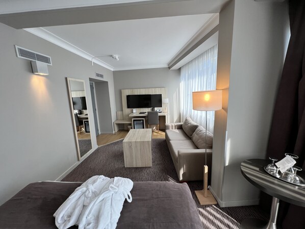 Una habitación de hotel moderna con una cama grande, un sofá, un escritorio con televisor y un comedor.