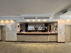 Un espace d’accueil doté d’un comptoir en marbre, de tableaux encadrés et offrant une vue dégagée sur le hall d’entrée.