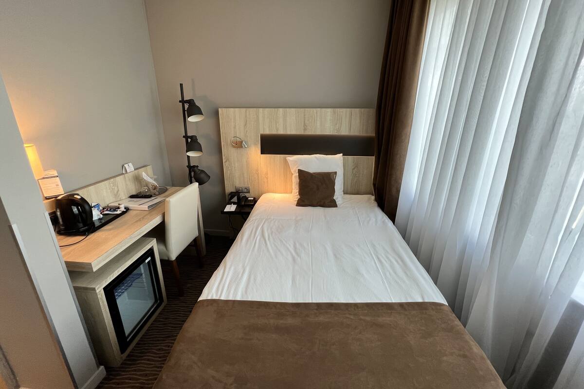 Una habitación de hotel con una cama, un escritorio con una computadora, una lámpara y un televisor.