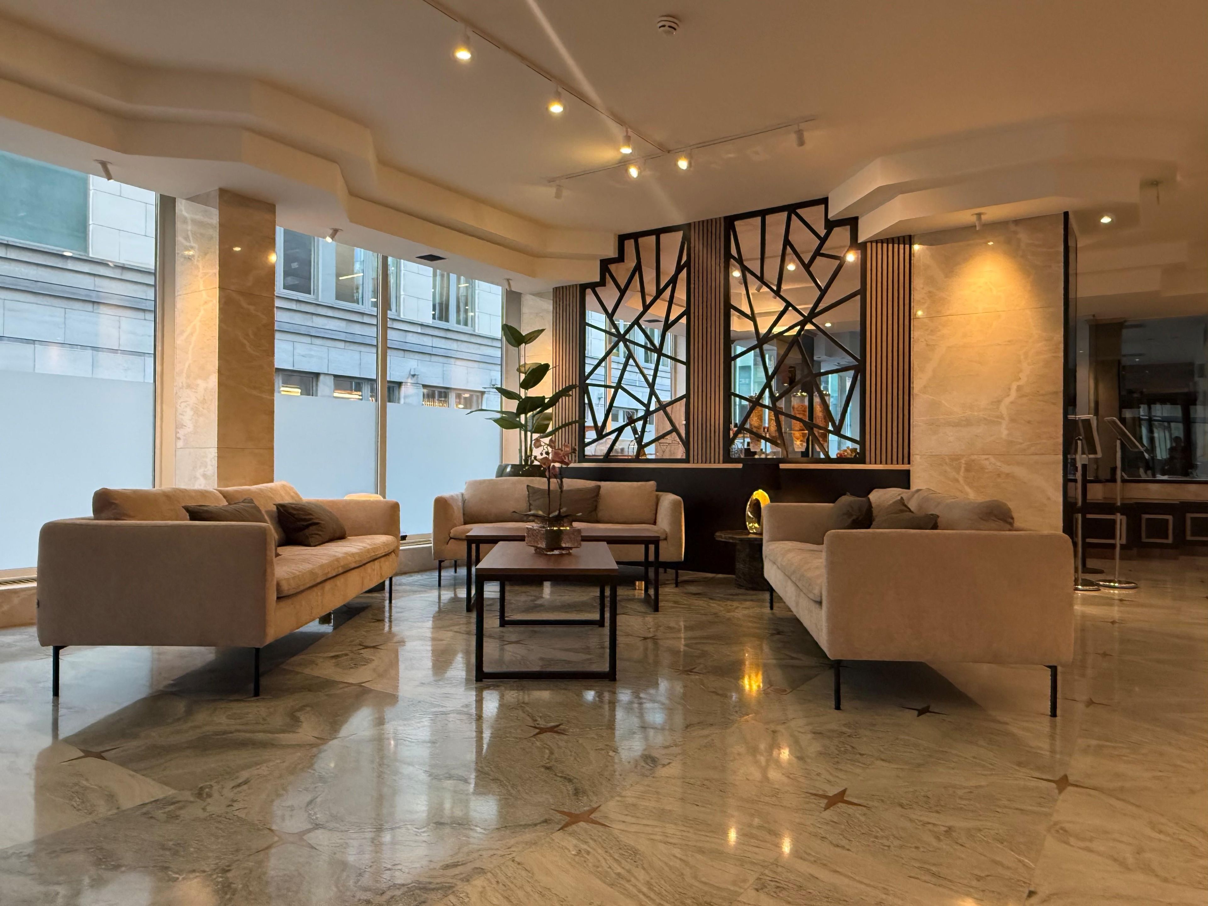 A modern hotel lobby with a marble floor, sofas, a coffee table, and a decorative partition with geometric patterns.