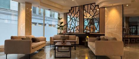 A modern hotel lobby with a marble floor, sofas, a coffee table, and a decorative partition with geometric patterns.