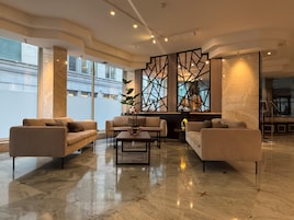 Un moderno vestíbulo de hotel con piso de mármol, sofás, una mesa de centro y un separador decorativo con motivos geométricos.