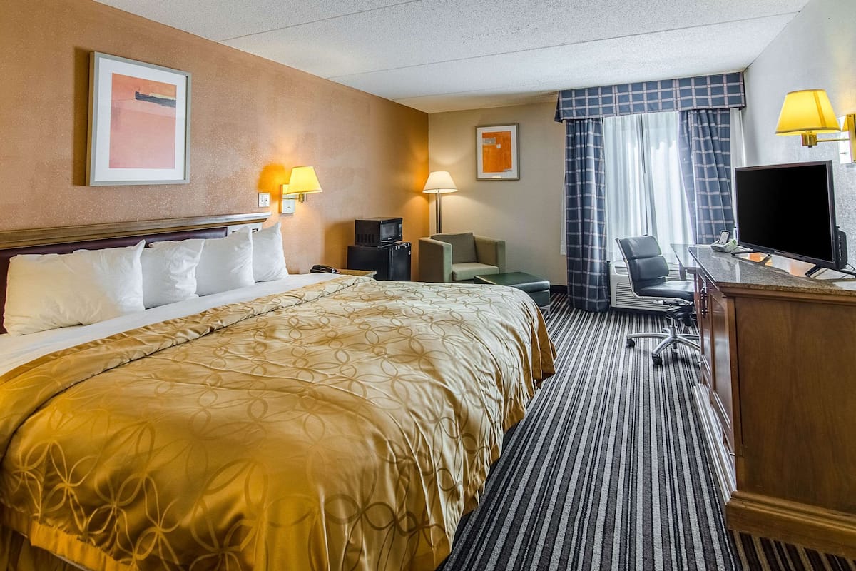 A hotel room with a large bed, a desk with a computer, a chair, and a TV.