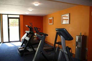 Un gimnasio con cintas de correr, dispensador de agua y una puerta que da al exterior.
