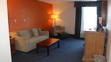 A room with a sofa, a chair, a small table, a lamp, a wooden cabinet, and a window with curtains.