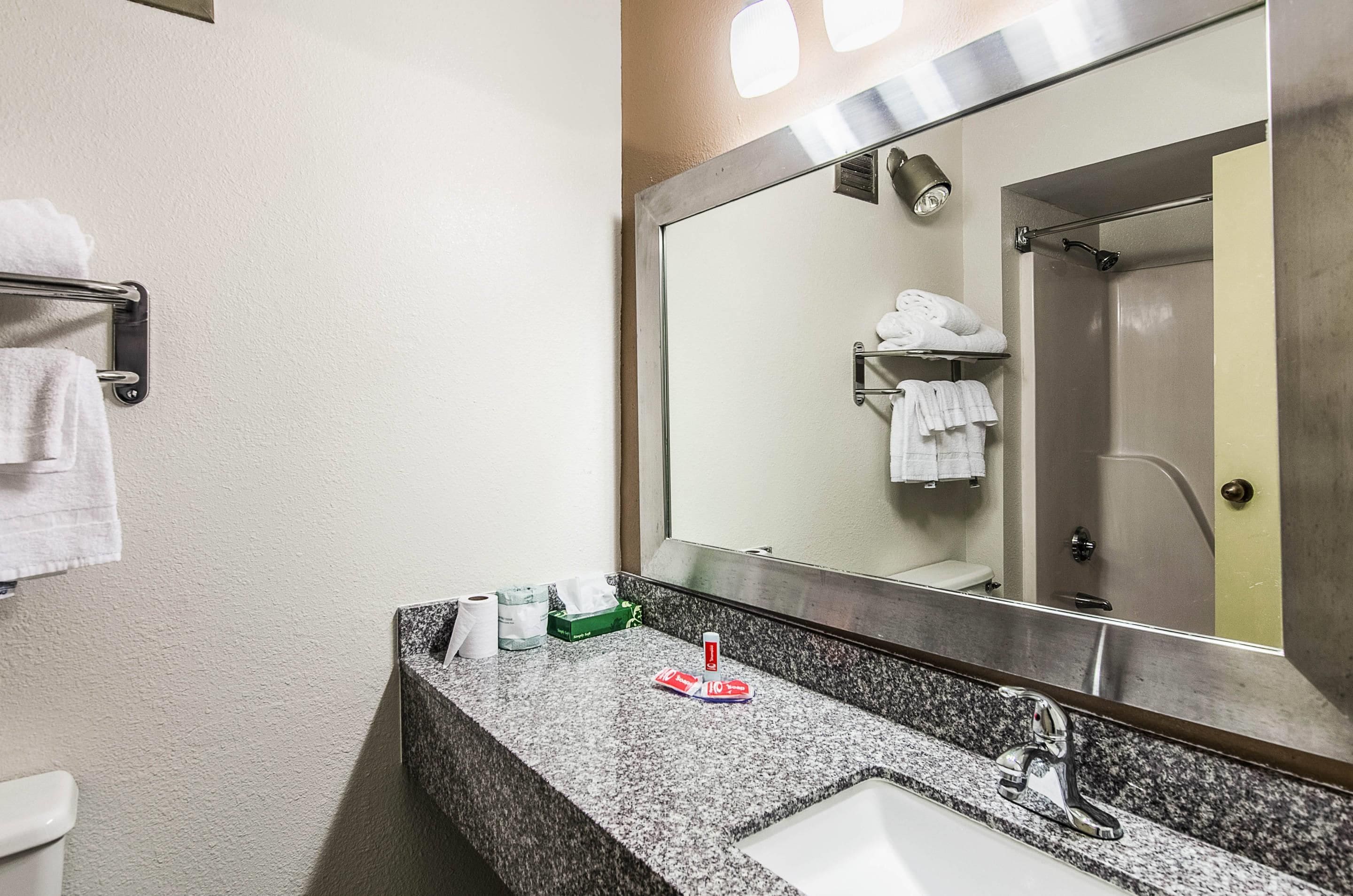 Un baño con lavamanos, espejo, toallero y una ducha que se ve en el reflejo.