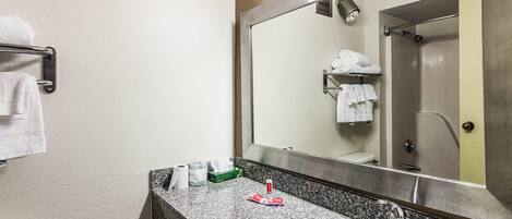 Un baño con lavamanos, espejo, toallero y una ducha que se ve en el reflejo.
