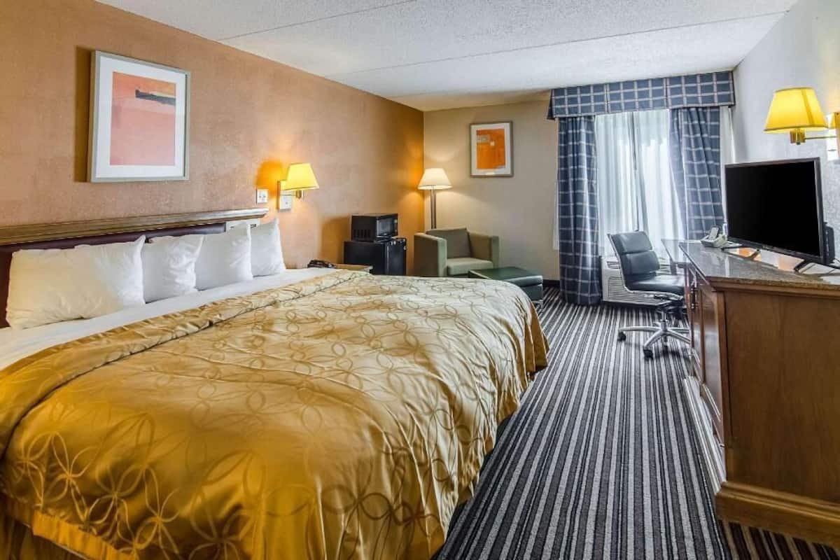 A hotel room with a large bed, a desk with a computer, a TV, and a chair.