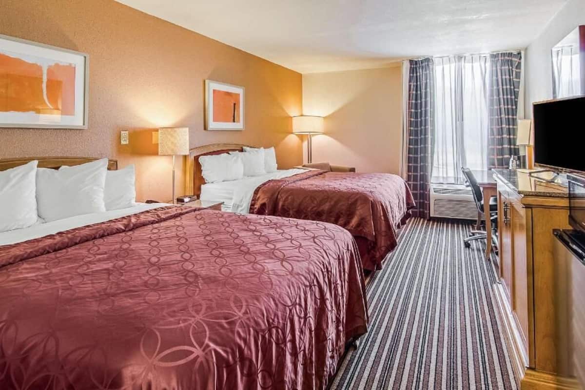 A hotel room with two beds, a desk, a television, and a window with curtains.