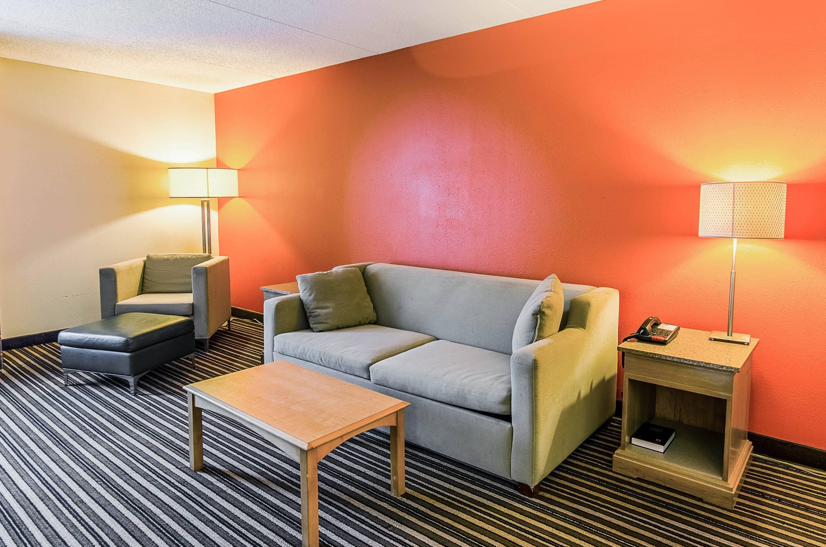 A hotel room with a sofa, armchair, and a small table. There are two lamps and a telephone on a side table.