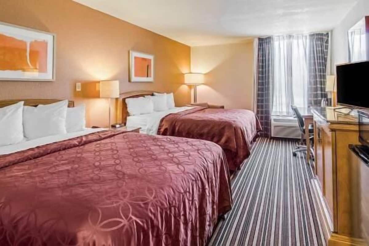 A hotel room with two beds, a desk, a television, and a window with curtains.