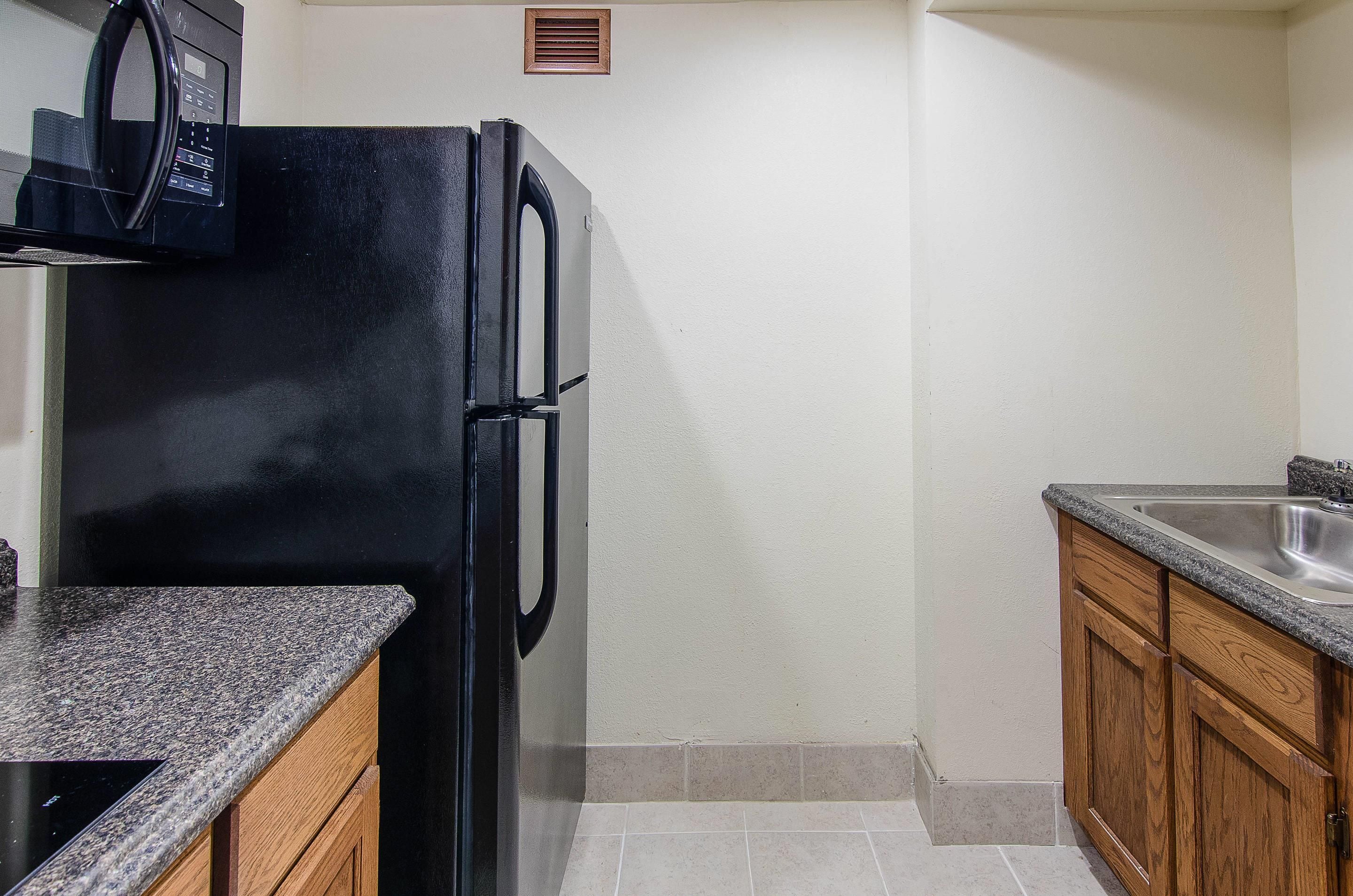 A compact kitchen with a black refrigerator, a granite countertop, and wooden cabinets.