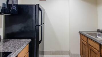 A compact kitchen with a black refrigerator, a granite countertop, and wooden cabinets.