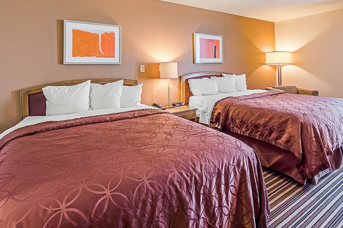 A hotel room with two beds, each with a patterned bedspread, a nightstand with a lamp, and framed artwork on the wall.