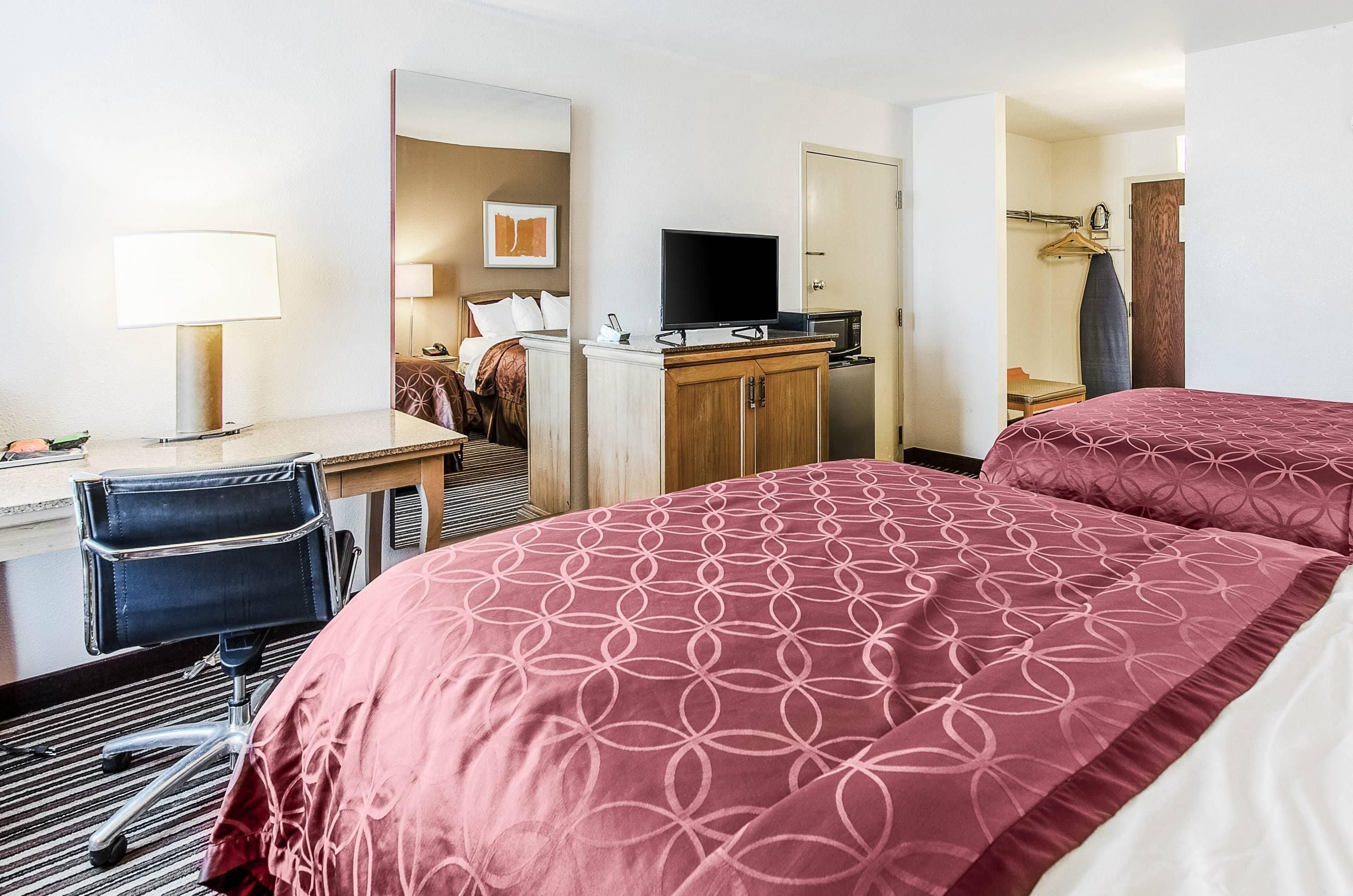 A hotel room with a bed, desk, chair, television, and a wardrobe.