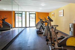 Academia com máquinas de cardio, bebedouro e parede de vidro com vista para o exterior.