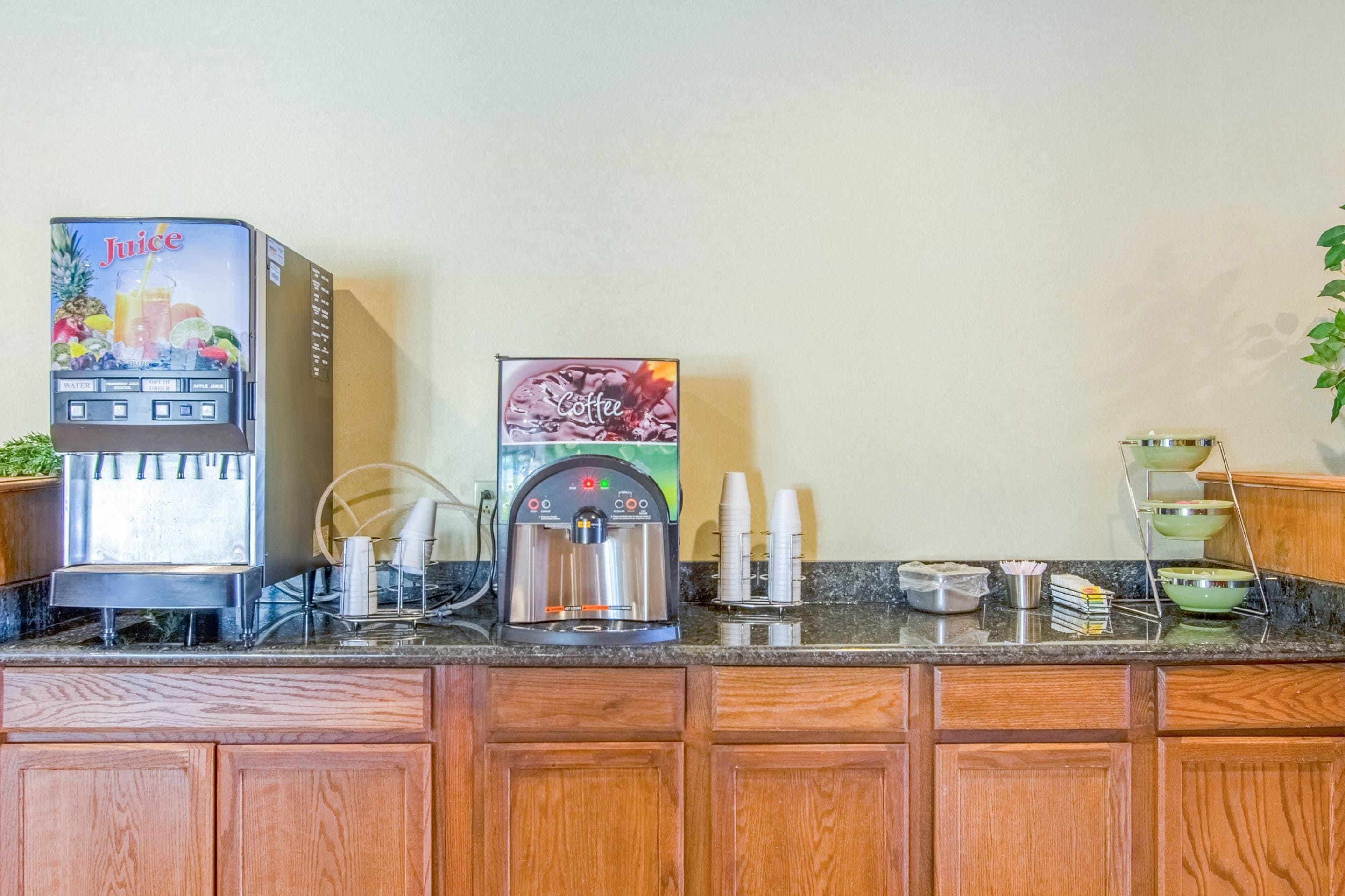A coffee station with a juice dispenser and a coffee machine, along with cups and a small plant.