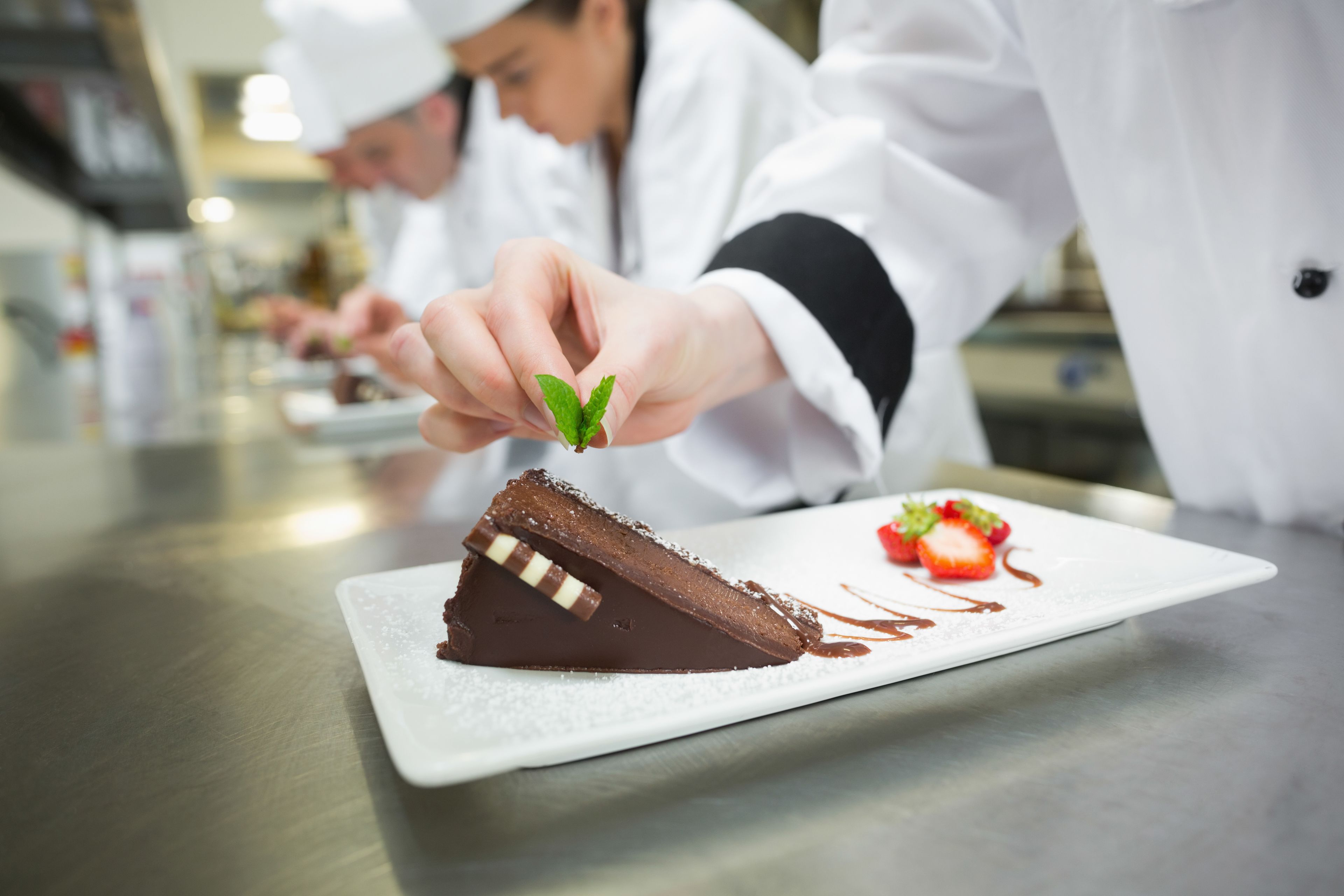 A chef garnishing a chocolate dessert with mint leaves.