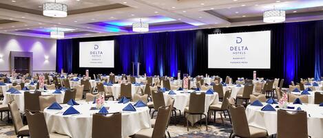 A large conference room with multiple round tables, each set with white tablecloths and blue napkins.
